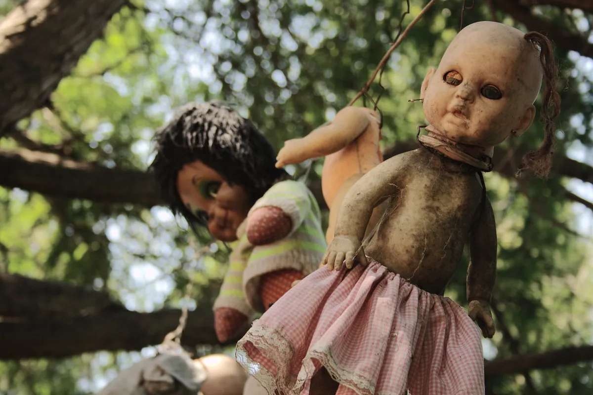 Two weathered dolls hanging from a tree branch on the Island of the Dolls in Xochimilco, one in a pink checked dress with a cracked face