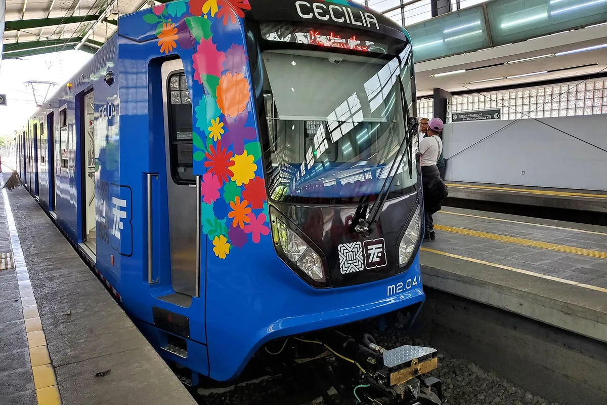 A blue and white light rail train decorated with flowers standing at a Xochimilco station platform
